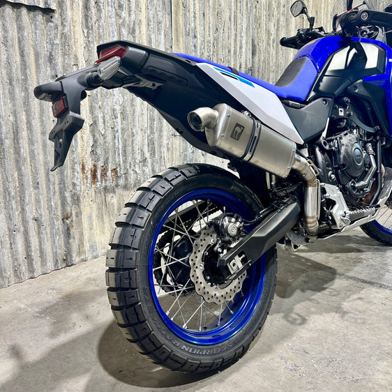 A Yamaha 700 Tenere motorcycle with a n Enduro bend high exhaust system by Camel ADV Products, displayed indoors with a logo in the background.